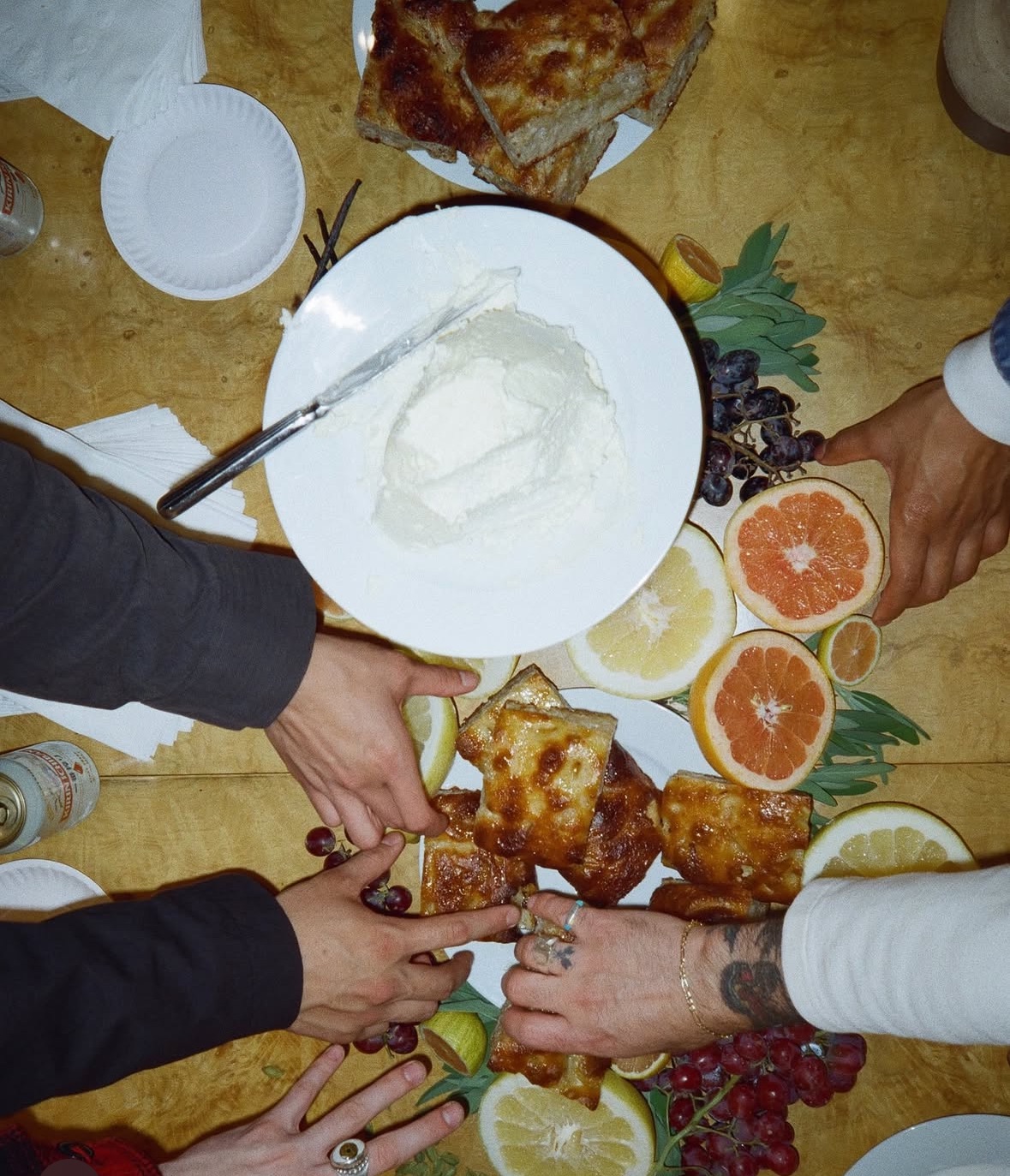 Intimate grazing table scene with hands reaching for whipped ricotta, focaccia, and fresh citrus