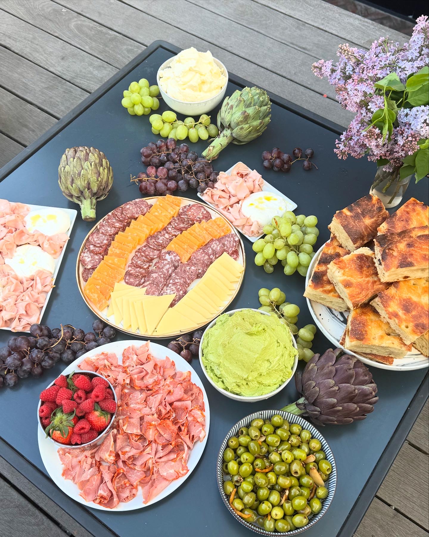 Elaborate grazing table with charcuterie, artichokes, cheese, focaccia and fresh fruits on dark slate