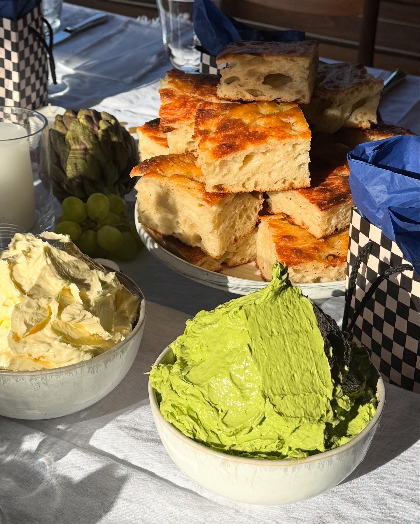 Close-up of golden focaccia bread with green and white spreads, artichokes and grapes