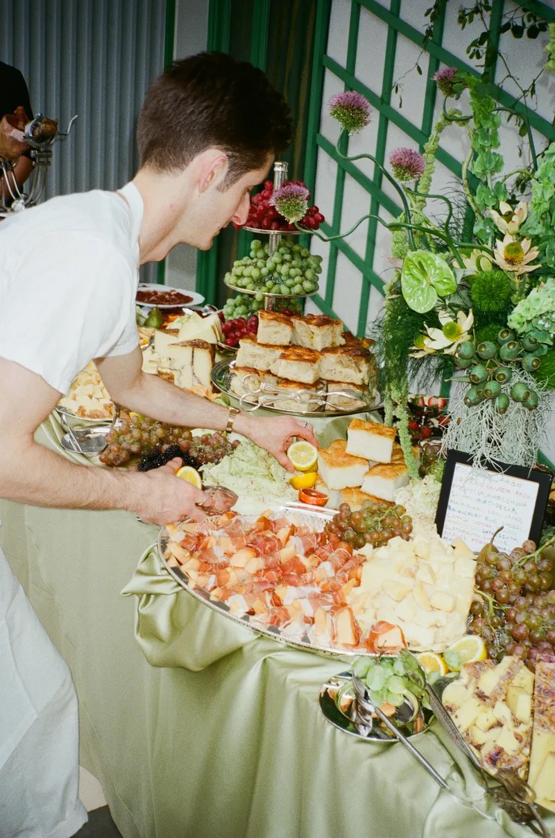 Chef arranging elegant tiered grazing table with charcuterie, cheese and beautiful floral arrangements